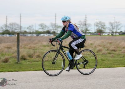 Bright woman cycling on paved trail with blue safety helmet and athletic gear during daytime.