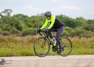 Bright yellow and black cyclist riding a road bike on open rural road during daytime.