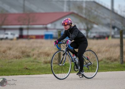 Brightly dressed woman riding a blue road bike outdoors on a cloudy day.