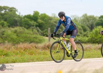 Bright yellow road bike on outdoor trail with smiling cyclist in blue jersey, green foliage background.