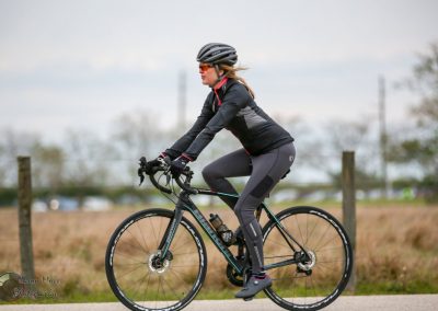 High-performance cycling woman wearing a helmet and athletic gear, riding a modern road bike outdoors.