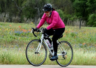 Bright pink jacket cyclist riding on a scenic trail with wildflowers in the background.