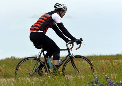 Bright cyclist riding the Bluebonnet Express bike through a scenic, flower-filled trail in Texas.