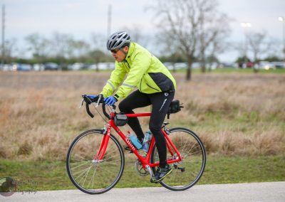 Bright yellow reflective cycling jacket on man riding red bike on paved trail.