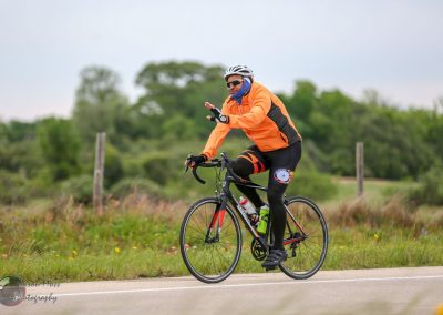 High-performance road cyclist riding on rural highway in weather gear, promoting Bluebonnet Express bike service.