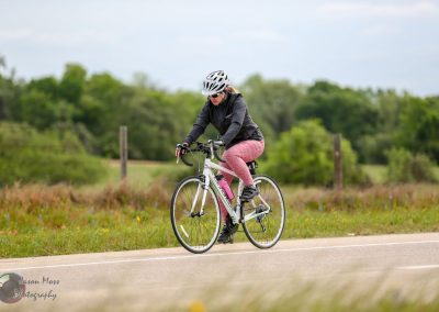 Bright woman cycling along scenic rural road on a white bike with pink accents during daytime.