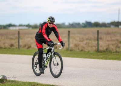 Velo cyclist riding on a paved trail in open countryside during daytime.