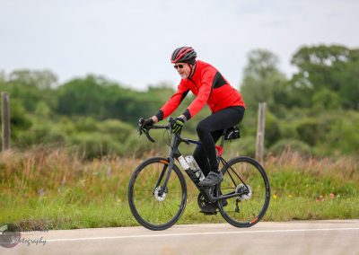 Man riding an electric bike with a red jacket on a rural road during daytime.