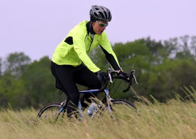 Vibrant cyclist in yellow jacket riding a bike through grassy field on Bluebonnet Express trail.