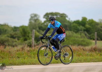 Vibrant cyclist riding on scenic rural road during daytime, promoting Bluebonnet Express cycling event.