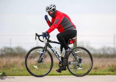Vegan cyclist wearing a red jacket on a road bike with a scenic outdoor background.