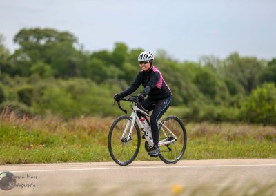 Women cycling on scenic outdoor trail with bike helmet, promoting Bluebonnet Express cycling events and bike safety.