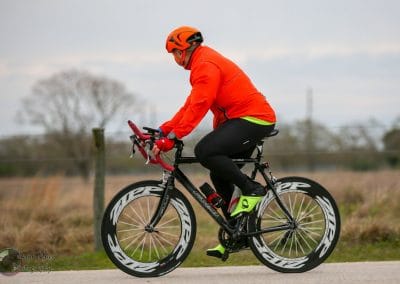 Fast cyclist riding a road bike with Zipp wheelset on a rural road, promoting Bluebonnet Express.