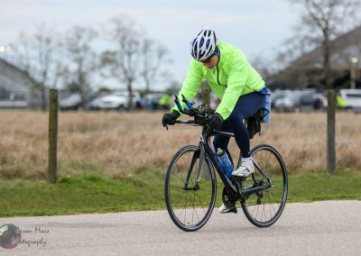 High-performance road cyclist riding on a track during daytime, wearing neon yellow jacket and helmet.