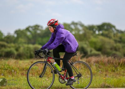 Vibrant cyclist riding through scenic outdoor countryside on a black and red bike with a purple jacket and helmet.