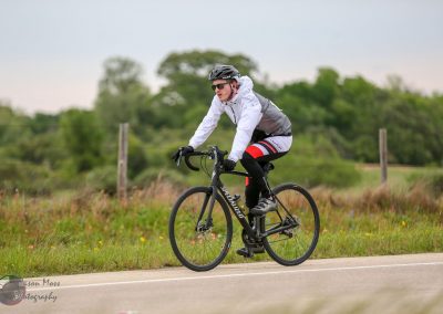 High-performance cyclist riding a Specialized road bike on scenic countryside road.