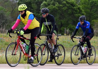 Brightly dressed cyclists riding through a scenic field with wildflowers in the background.