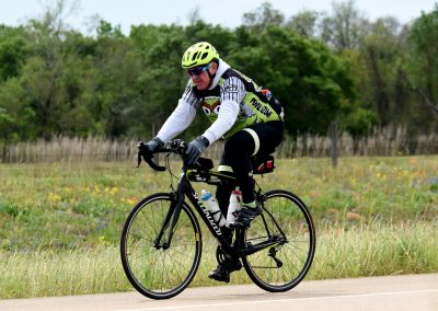 Bright yellow helmet and cycling gear on man riding a road bike through scenic countryside, promoting cycling adventure.