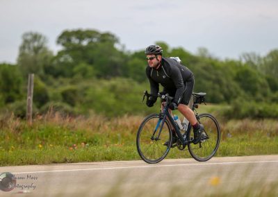 Velo cyclist riding on scenic rural road with lush green trees in the background.