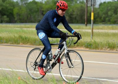 Bright blue HP cycling apparel worn by a cyclist riding on rural road for Bluebonnet Express event.