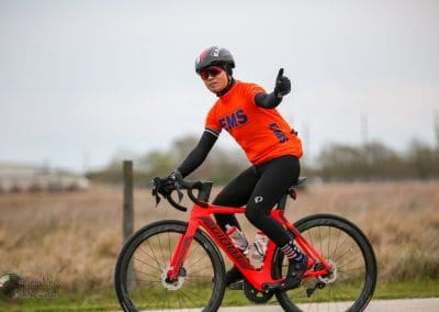 Vibrant cyclist riding a red bike outdoors with a blue "EMS" jersey and giving a thumbs-up.