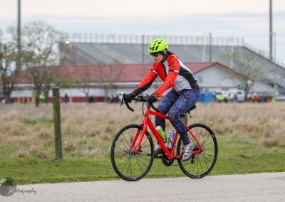 Bright red bike with a female cyclist riding outdoors in casual athletic wear.
