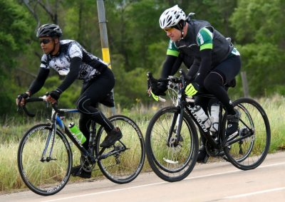 Efficient cyclists riding on rural road with green trees in background.
