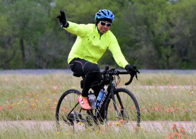 Vibrant cyclist in bright yellow jacket biking through grassy wildflower field on a clear day.