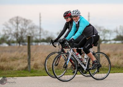Smiling women riding bikes outdoors, enjoying cycling adventure with Bluebonnet Express.