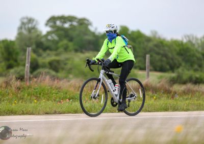 Bright green biking jacket and helmet on a cyclist riding through scenic outdoor trail, promoting Bluebonnet Express rides.