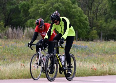 High-visibility cyclist in neon jacket riding with teammate along scenic countryside route.
