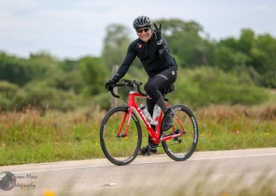 Vibrant cyclist riding a red bike on a scenic country road, capturing the spirit of Bluebonnet Express cycling event.
