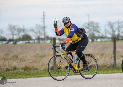 Colorful cyclist wearing helmet and sunglasses making peace sign during Bluebonnet Express ride.