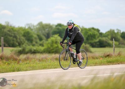Vibrant cyclist riding on road through open countryside with green trees and cloudy sky.