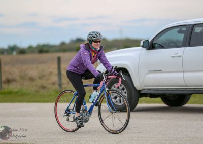 Vibrant woman cyclist riding on rural road with Bluebonnet Express branding in background.