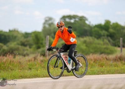 Cyclist in orange jacket riding a bicycle through rural landscape during daytime.