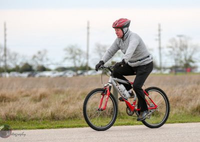 Cyclist riding a mountain bike in an outdoor park on a paved trail.