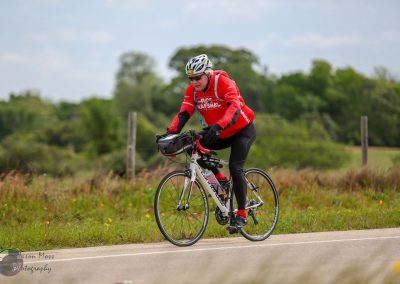 Bright red cyclist outfit on a scenic bike ride along a rural trail, promoting Bluebonnet Express cycling event.