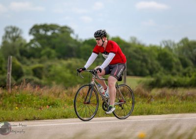 High-performance cyclist riding on rural road, promoting Bluebonnet Express bike service, outdoor cycling event, fitness, and adventure.