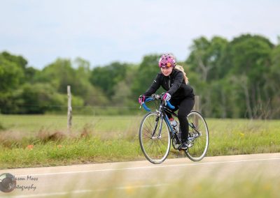 Girl riding a bicycle on a rural trail in Texas during daytime, wearing safety gear.