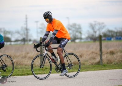 Bright orange cyclist jersey riding on a road bike with a rural background.