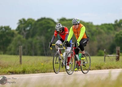 Brightly dressed cyclists riding on a paved rural road in a scenic outdoor setting.