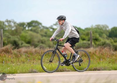Young man riding a black electric bike outdoors in green countryside, showcasing eco-friendly transportation.