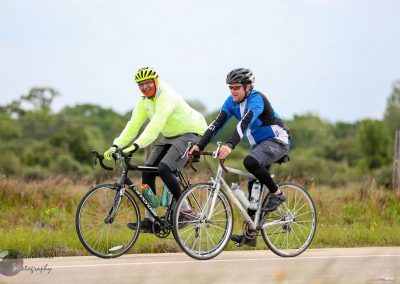Two cyclists enjoying a ride on the scenic Bluebonnet Express trail with lush greenery in the background.