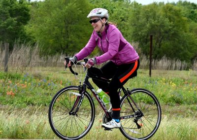 Vibrant woman riding a bike through scenic countryside with wildflowers and greenery.
