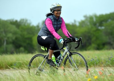 Vibrant woman cycling outdoors in scenic green landscape with bluebonnet flowers.