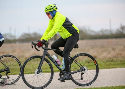 Bright yellow cycling jacket and helmet on a man riding a sleek black road bike outdoors.
