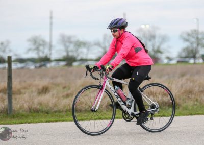 Bright pink cycling jacket with helmet and sunglasses on a woman riding a road bike during daytime.