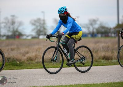 Vegan cyclist wearing blue jacket and helmet riding a black road bike outdoors.