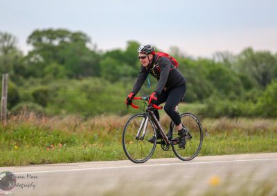 Velo cyclist riding on rural road with scenic greenery and open fields, promoting outdoor biking adventures.